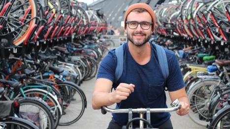 Aanzicht van een grote fietsenstalling met een jonge man die net wil wegfietsen.